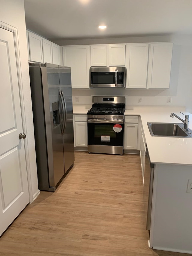 318 Riverwood Village Ln, Sealy, TX 77474 - kitchen featuring appliances with stainless steel finishes, a sink, light countertops, light wood finished floors, and white cabinetry