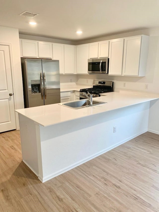 318 Riverwood Village Ln, Sealy, TX 77474 - kitchen with appliances with stainless steel finishes, a peninsula, light wood-style floors, light countertops, and white cabinets