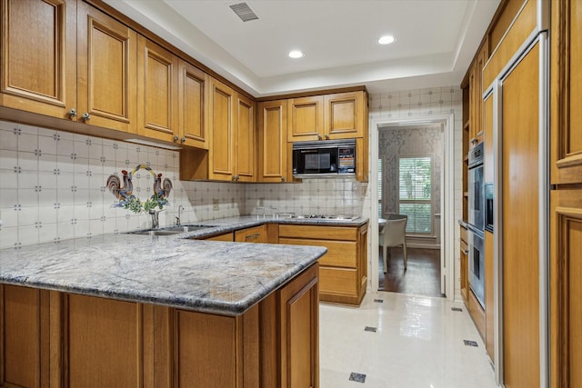 2628 Glen Haven Blvd, Houston, TX 77025 - kitchen featuring black microwave, brown cabinetry, a peninsula, light stone counters, and backsplash