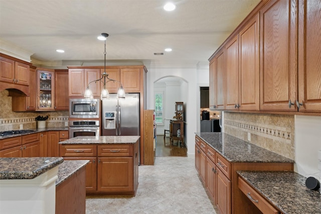 3602 Lindhaven Dr, Pearland, TX 77584 - kitchen featuring stainless steel appliances, arched walkways, brown cabinetry, dark stone countertops, and glass insert cabinets