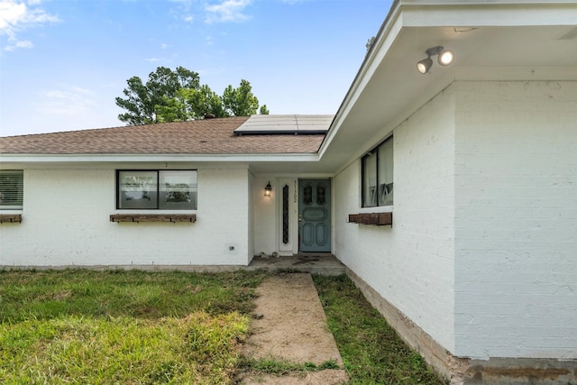 31302 Wisteria Rd, Magnolia, TX 77355 - doorway to property with roof mounted solar panels, a shingled roof, and brick siding