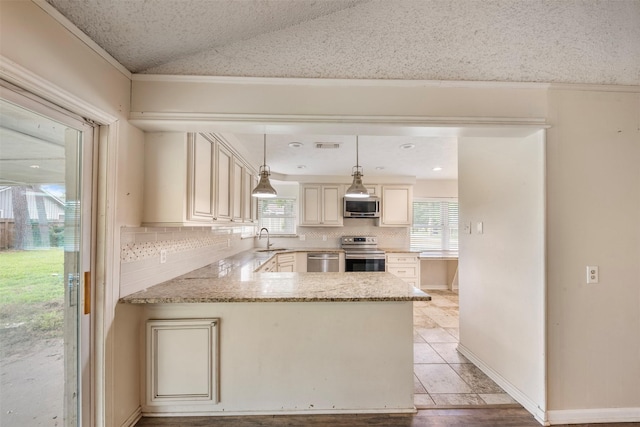 31302 Wisteria Rd, Magnolia, TX 77355 - kitchen featuring appliances with stainless steel finishes, cream cabinets, decorative backsplash, lofted ceiling, and light stone counters