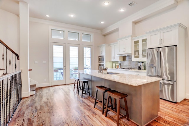 1348 W 25th St, Houston, TX 77008 - kitchen with stainless steel appliances, crown molding, a kitchen island with sink, a breakfast bar, and light stone counters