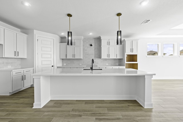 30419 Bermuda Hallow Bnd, Fulshear, TX 77423 - kitchen featuring a sink, a spacious island, backsplash, wood finished floors, and white cabinetry