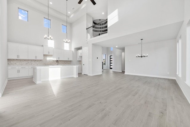 24727 Lobelia Garden Ln, Katy, TX 77493 - unfurnished living room featuring a chandelier, ceiling fan, light wood-type flooring, a towering ceiling, and baseboards