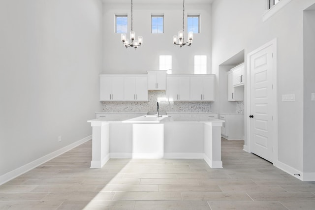 24727 Lobelia Garden Ln, Katy, TX 77493 - kitchen with a chandelier, a high ceiling, an island with sink, light wood finished floors, and white cabinetry