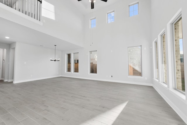 24727 Lobelia Garden Ln, Katy, TX 77493 - unfurnished living room with a ceiling fan, a towering ceiling, baseboards, light wood-type flooring, and a chandelier