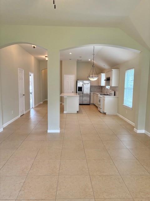 19119 Field Cottage Ln, Richmond, TX 77407 - kitchen featuring stainless steel fridge with ice dispenser, white range with gas stovetop, light tile patterned floors, arched walkways, and vaulted ceiling