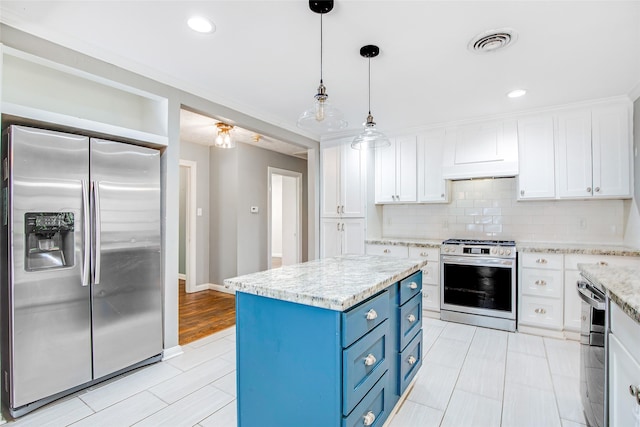 606 N Main St, Dayton, TX 77535 - kitchen with appliances with stainless steel finishes, blue cabinets, white cabinetry, decorative backsplash, and hanging light fixtures