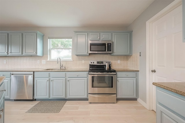 15251 Weeping Cedar Ln, Houston, TX 77084 - kitchen featuring stainless steel appliances, a sink, decorative backsplash, light wood-type flooring, and gray cabinetry