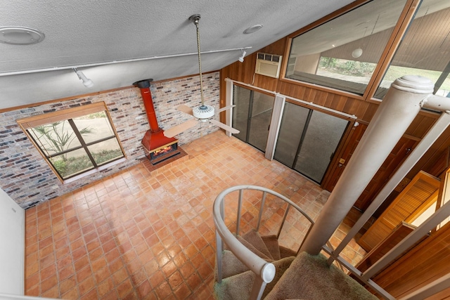 9809 Neuens Rd, Houston, TX 77080 - unfurnished living room with a textured ceiling, a wood stove, wood walls, and vaulted ceiling