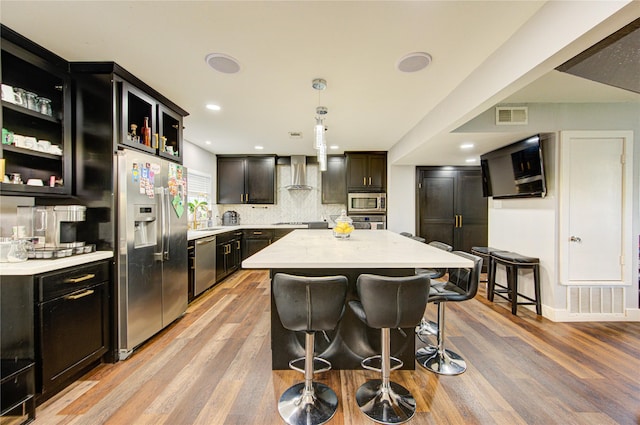 2246 Triway Ln, Houston, TX 77043 - kitchen featuring stainless steel appliances, wall chimney exhaust hood, light wood-style floors, a kitchen breakfast bar, and recessed lighting