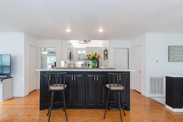6840 County Road 659, Brazoria, TX 77422 - kitchen with a kitchen breakfast bar, wooden walls, light countertops, dark cabinetry, and light wood finished floors