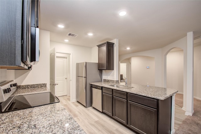 10699 Lost Maples Dr, Cleveland, TX 77328 - kitchen featuring stainless steel appliances, arched walkways, a sink, dark brown cabinetry, and a peninsula