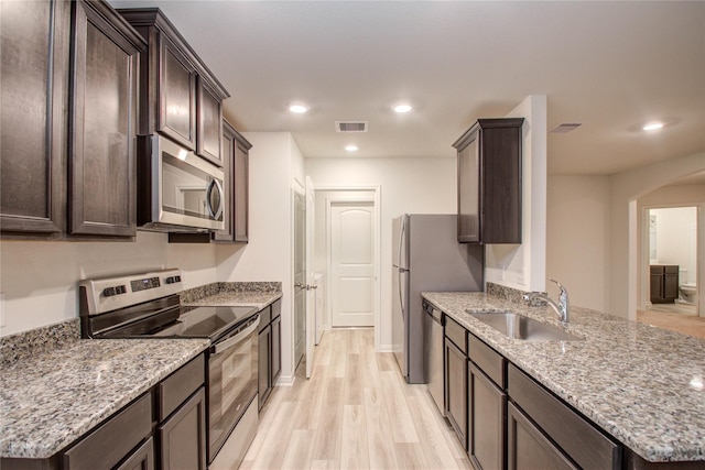 10699 Lost Maples Dr, Cleveland, TX 77328 - kitchen with stainless steel appliances, a sink, dark brown cabinets, arched walkways, and light wood-style flooring