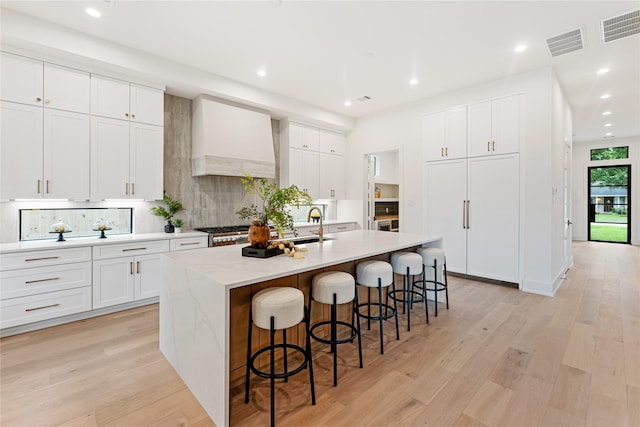 1741 Chippendale Rd, Houston, TX 77018 - kitchen with premium range hood, a center island with sink, a kitchen breakfast bar, decorative backsplash, and light wood-type flooring