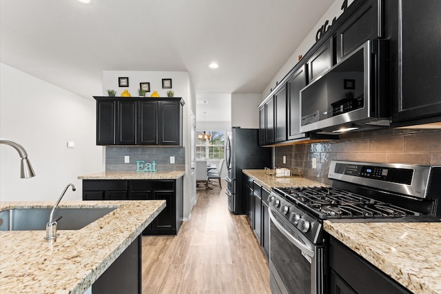 11375 Dawn Beach Ln, Conroe, TX 77304 - kitchen with appliances with stainless steel finishes, dark cabinetry, a sink, light wood-style flooring, and light stone countertops