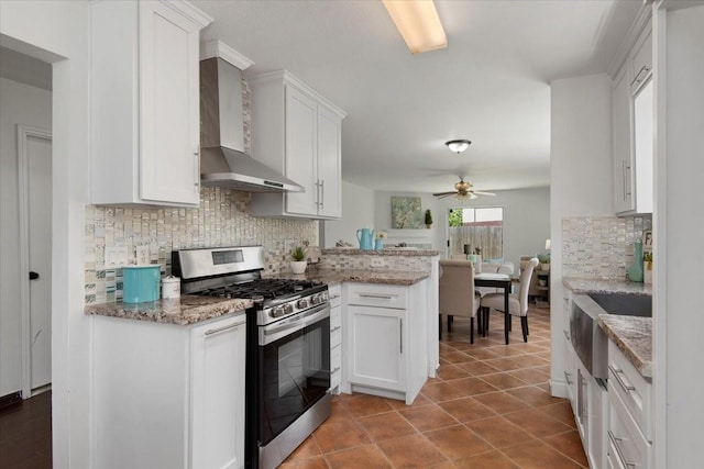 8702 Cold Lake Dr, Houston, TX 77088 - kitchen with stainless steel gas range, wall chimney exhaust hood, decorative backsplash, white cabinets, and a ceiling fan
