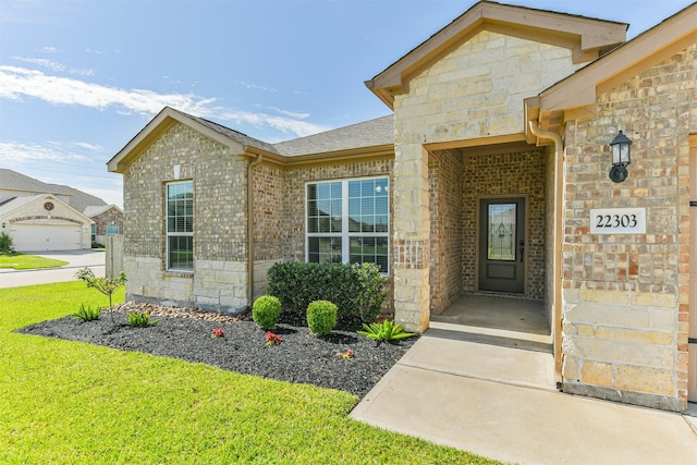 22303 Bauer Garden Dr, Hockley, TX 77447 - view of exterior entry featuring stone siding, a yard, brick siding, and roof with shingles
