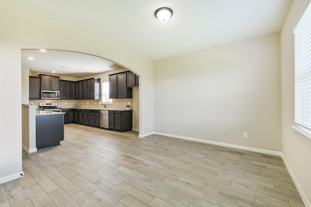 22303 Bauer Garden Dr, Hockley, TX 77447 - kitchen featuring appliances with stainless steel finishes, arched walkways, a sink, backsplash, and light wood-style floors