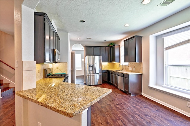 20610 Arrow Falls Ln, Richmond, TX 77407 - kitchen featuring appliances with stainless steel finishes, a peninsula, arched walkways, decorative backsplash, and a textured ceiling