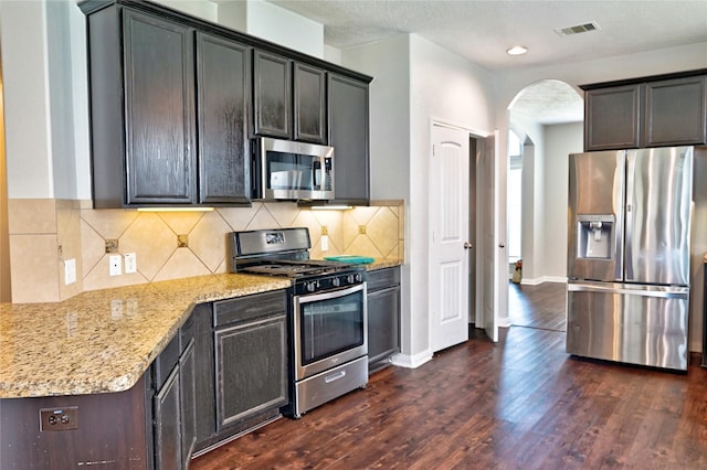 20610 Arrow Falls Ln, Richmond, TX 77407 - kitchen featuring appliances with stainless steel finishes, arched walkways, light stone countertops, and dark wood-type flooring