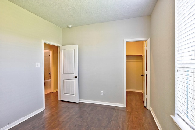 20610 Arrow Falls Ln, Richmond, TX 77407 - unfurnished bedroom with dark wood finished floors, a walk in closet, multiple windows, baseboards, and a textured ceiling