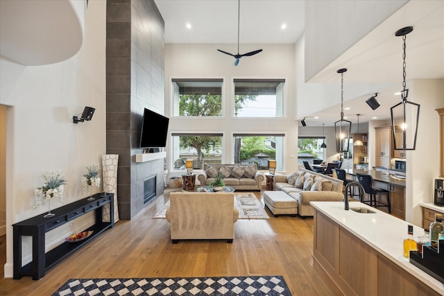 4019 Drummond St, Houston, TX 77025 - living room featuring a high ceiling, light wood-type flooring, a fireplace, and a ceiling fan