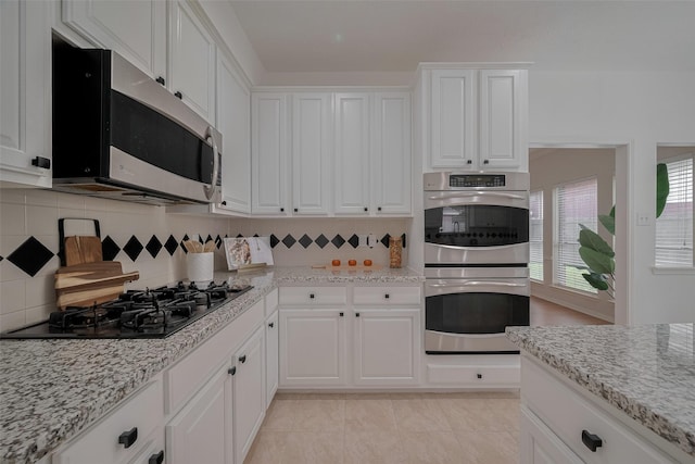 11943 Natural Bridges Ln, Sugar Land, TX 77498 - kitchen featuring appliances with stainless steel finishes, white cabinetry, decorative backsplash, and light stone countertops