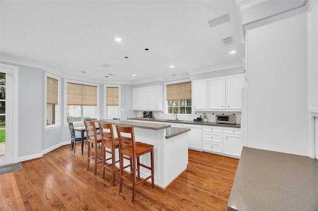 3509 Gramercy St, Houston, TX 77025 - kitchen featuring crown molding, a kitchen bar, a center island, light wood finished floors, and white cabinetry