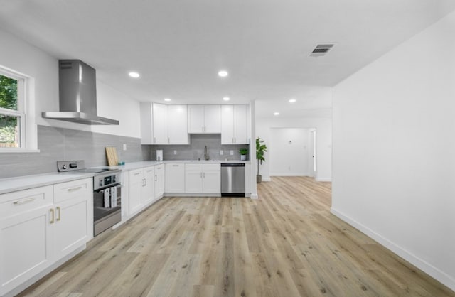 3906 Simsbrook Dr, Houston, TX 77045 - kitchen featuring wall chimney exhaust hood, appliances with stainless steel finishes, tasteful backsplash, white cabinetry, and light wood-style flooring