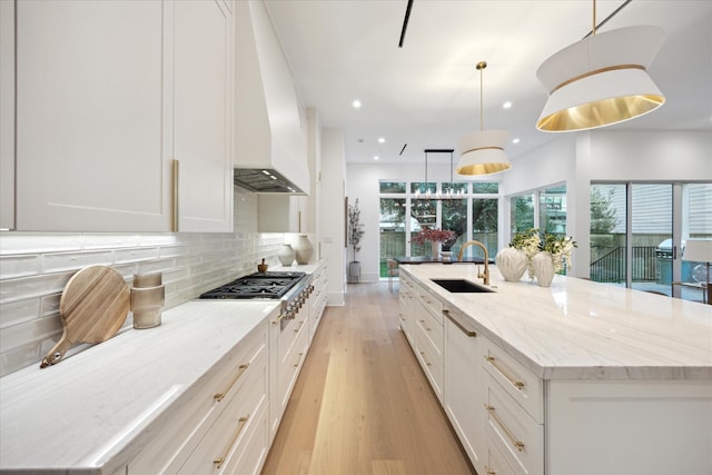 806 Holton St, Bellaire, TX 77401 - kitchen with a sink, premium range hood, stainless steel gas cooktop, light wood-style flooring, and a large island