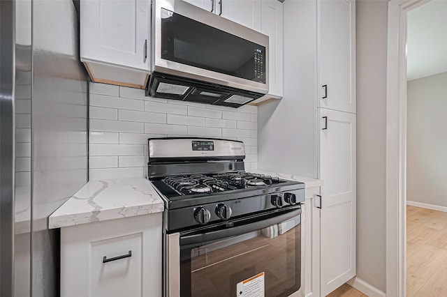 10623 Dunvegan Way, Houston, TX 77013 - kitchen with black range with gas stovetop, stainless steel microwave, light wood-style floors, and tasteful backsplash