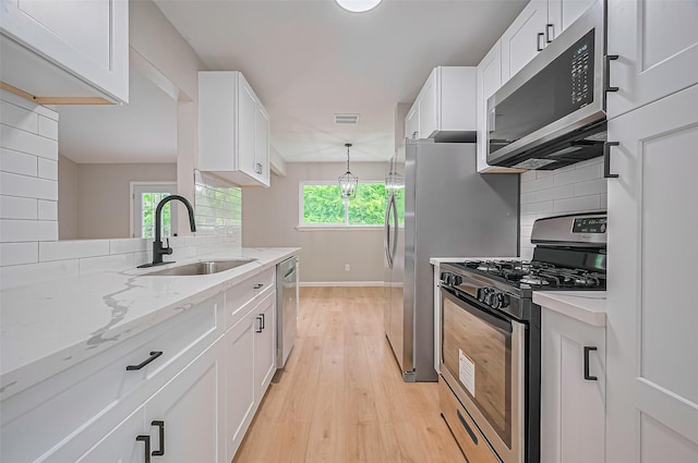 10623 Dunvegan Way, Houston, TX 77013 - kitchen with stainless steel appliances, a sink, light wood-style flooring, white cabinetry, and baseboards