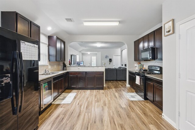 12911 Italian Cypress Trl, Houston, TX 77044 - kitchen featuring black appliances, beverage cooler, arched walkways, light wood-style flooring, and a peninsula