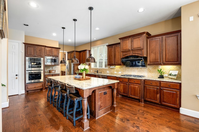6019 Majestic Pines Dr, Houston, TX 77345 - kitchen with stainless steel appliances, dark wood-style flooring, a kitchen bar, tasteful backsplash, and a kitchen island with sink