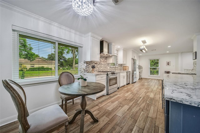 963 Thornton Rd, Houston, TX 77018 - kitchen featuring stainless steel appliances, wall chimney range hood, a chandelier, white cabinets, and light wood-type flooring
