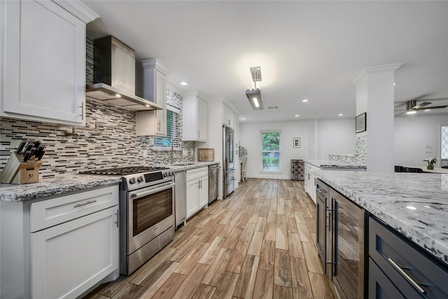 963 Thornton Rd, Houston, TX 77018 - kitchen with wall chimney range hood, stainless steel appliances, beverage cooler, light wood-style floors, and white cabinetry