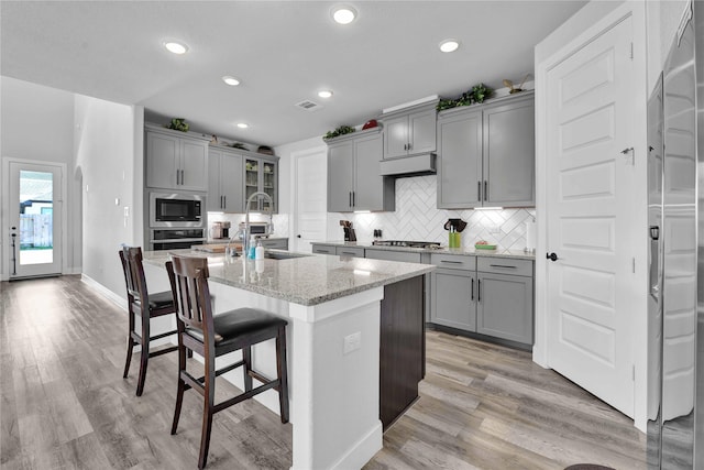 11930 Mccallister Run Dr, Humble, TX 77346 - kitchen with gray cabinetry, appliances with stainless steel finishes, a kitchen bar, light wood-style flooring, and recessed lighting