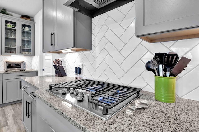 11930 Mccallister Run Dr, Humble, TX 77346 - kitchen featuring stainless steel gas stovetop, backsplash, glass insert cabinets, light stone countertops, and range hood