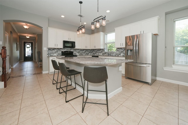 16826 Paynes Creek Dr, Cypress, TX 77433 - kitchen with black microwave, stainless steel fridge with ice dispenser, stove, arched walkways, and light tile patterned flooring