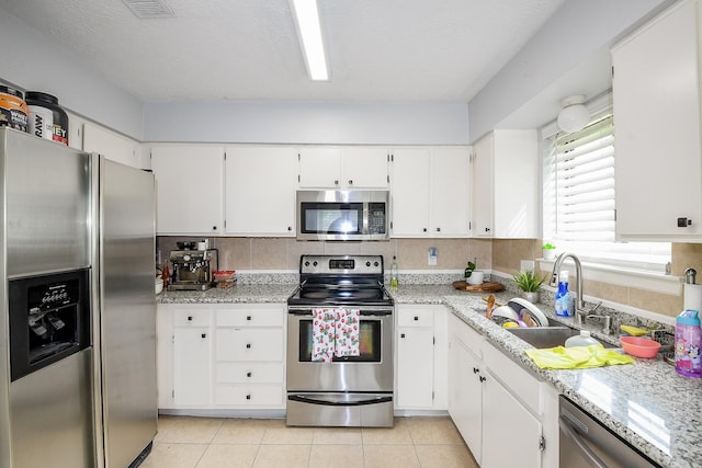 4623 Tealgate Dr, Spring, TX 77373 - kitchen featuring appliances with stainless steel finishes, a sink, white cabinetry, light tile patterned floors, and light stone counters