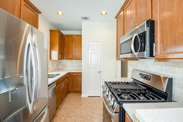 15027 Silhouette Ridge Dr, Humble, TX 77396 - kitchen featuring appliances with stainless steel finishes, tasteful backsplash, brown cabinetry, light tile patterned flooring, and recessed lighting
