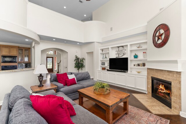 3610 Wellspring Lake Dr, Fulshear, TX 77441 - living area with arched walkways, a brick fireplace, dark wood-style flooring, a high ceiling, and built in features