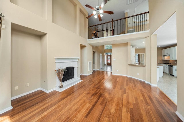26 Oakmont Ct, Jersey Village, TX 77064 - unfurnished living room featuring ceiling fan, light wood-style flooring, a high ceiling, a fireplace with raised hearth, and baseboards