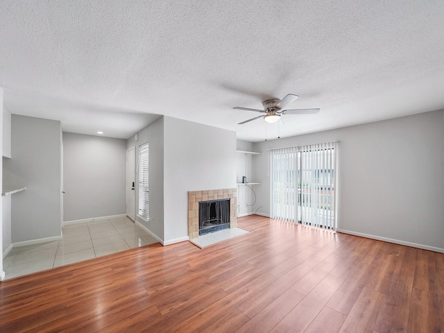 6633 W Airport Blvd Unit 1106, Houston, TX 77035 - unfurnished living room featuring ceiling fan, wood finished floors, a tiled fireplace, baseboards, and a textured ceiling