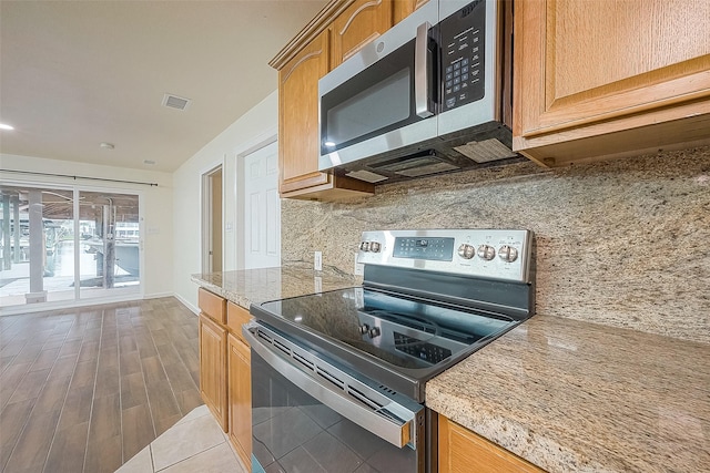 1407 Tiki Dr, Tiki Island, TX 77554 - kitchen featuring stainless steel appliances, light stone countertops, decorative backsplash, and wood finished floors