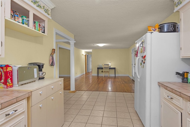 511 Northwood Dr, Conroe, TX 77303 - kitchen with tile counters, light tile patterned floors, white refrigerator with ice dispenser, a textured ceiling, and decorative columns
