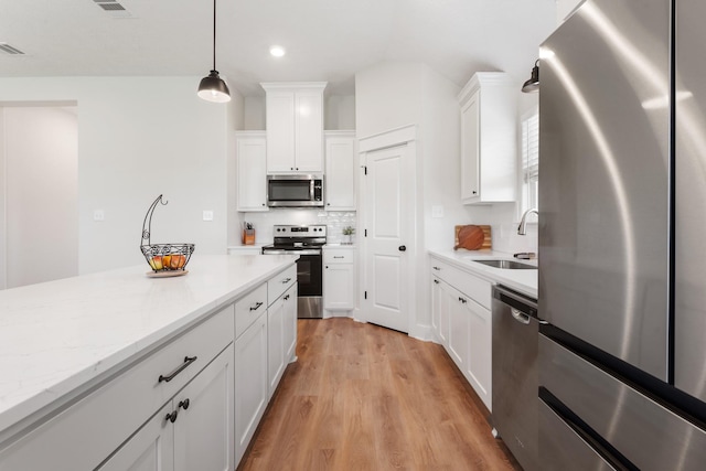 263 Brazos Bnd, Snook, TX 77879 - kitchen with stainless steel appliances, a sink, white cabinetry, hanging light fixtures, and light wood finished floors