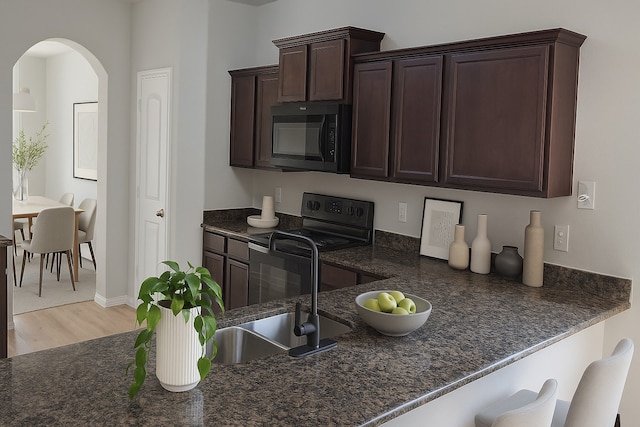2507 Ocean Cove Cir, Rosenberg, TX 77469 - kitchen with black appliances, light wood-style flooring, arched walkways, dark brown cabinetry, and dark stone counters